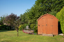 Devon, England, UK. 2021.  A Dutch Barn Style Garden Shed With Double Doors Standing With Patio, Tables And Chairs In An English Country Garden.