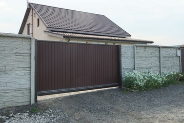 Wall Mural - one large closed brown metal gate and a long gray concrete fence wall on a rural street