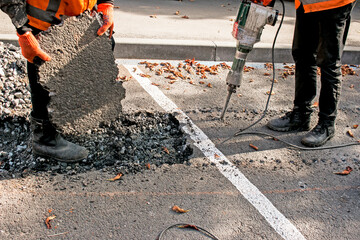 Workers remove a layer of old asphalt with a jackhammer on an autumn day.