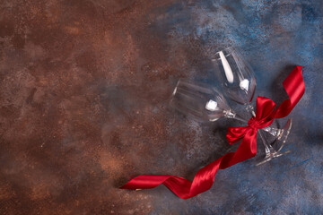 Canvas Print - Background of Valentines day celebration with two glasses and red ribbon on stone background with copy space, flat lay.