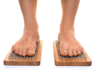 Close up photo of a male feet stand on a board with sharp nails over white background. Sadhu's board - practice yoga. Pain, trials, health, relaxation, cognition.