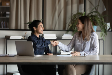 Canvas Print - Two smiling diverse young women corporate workers shake hands satisfied with successful cooperation making good deal. Millennial indian female employee handshake colleague appreciate for help in work