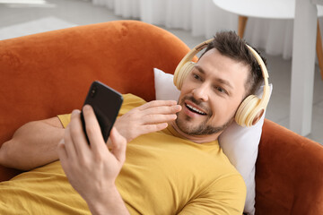 Canvas Print - Surprised man with phone and headphones lying on sofa