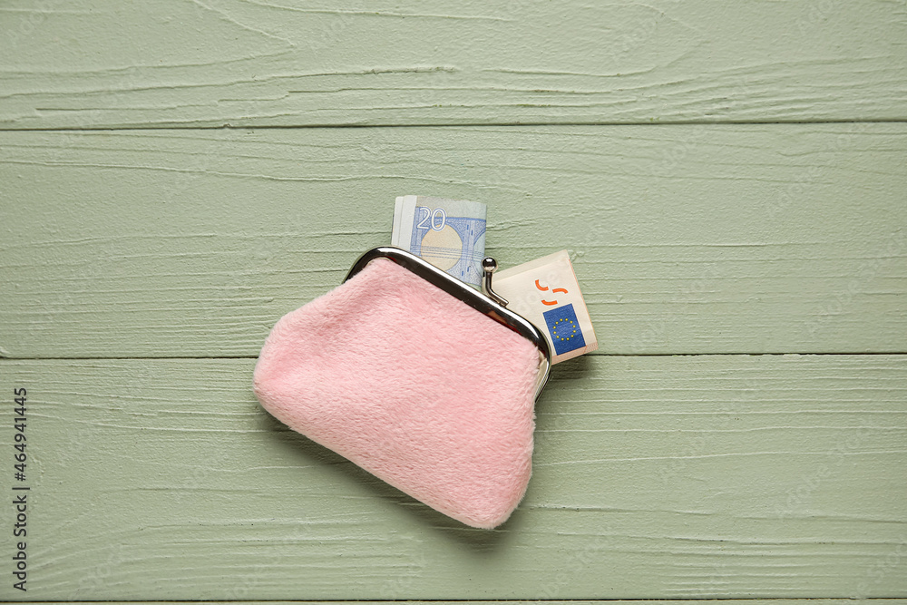 Pink wallet with banknotes on green wooden background
