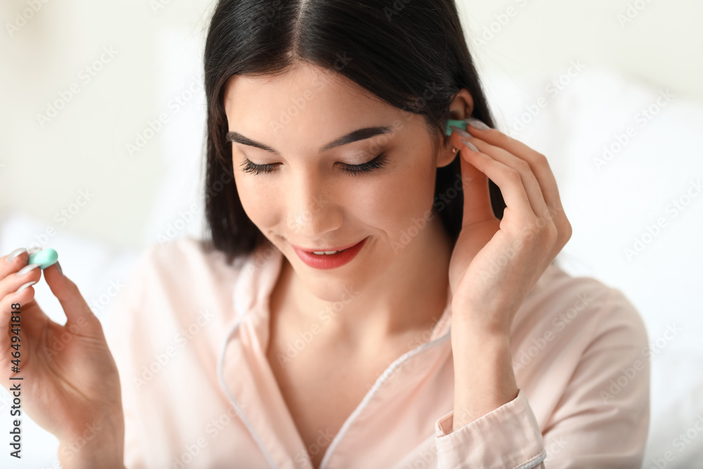 Pretty young woman putting blue ear plug in bedroom, closeup