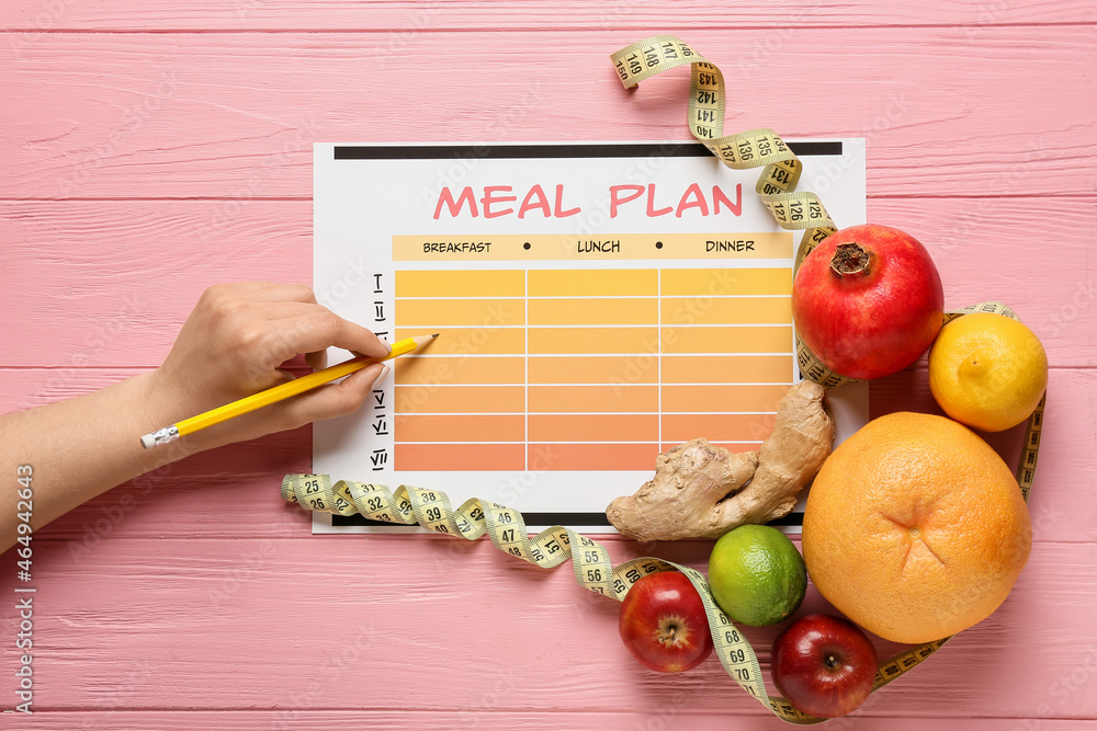 Woman making meal plan on color wooden background