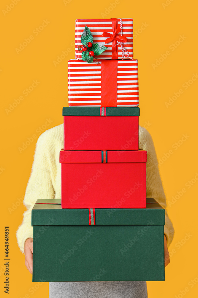Woman holding Christmas gift boxes on yellow background