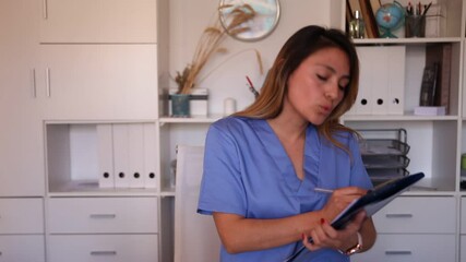 Wall Mural - Young latina woman doctor assistant standing in medical office making notes on clipboard