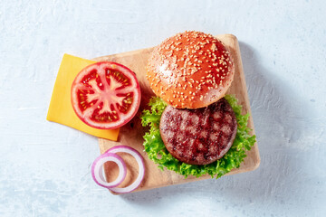 Burger ingredients, shot from above on a wooden board. Hamburger beef patty steak with vegetables, cheese, and a sesame bun bread