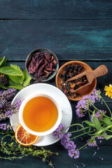 Poster - Herbal tea, top shot with a place for text. Herbs, flowers and fruit around a cup of tea on a dark rustic wooden background