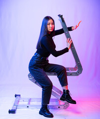 Wall Mural - portrait of a girl in black clothes with long black hair on a gray background. Eastern beauty with a transformer staircase. colored background, multicolored highlights on the model