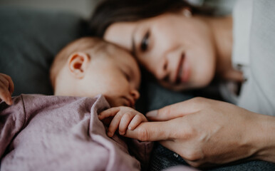 happy young mother touching her newborn baby girl, lying on sofa indoors at home.