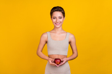 Wall Mural - Portrait of attractive cheerful girl holding fresh apple healthy diet nutrition calories isolated over bright yellow color background