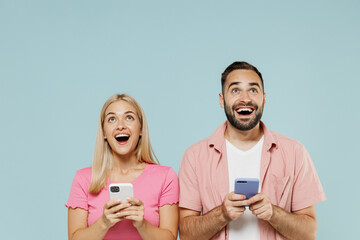 Wall Mural - Young couple two friends family man woman in casual clothes hold in hand use mobile cell phone look overhead on workspace together isolated on pastel plain light blue color background studio portrait.