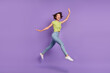 © deagreez - Photo of charming excited young woman dressed green t-shirt jumping walking waving arm empty space isolated purple color background