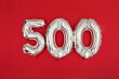 Silver balloon showing number 500 on red background. From above of silver shiny balloons demonstrating number 500 on red background with scattered glitter