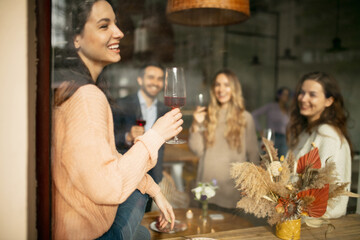 Wall Mural - Cropped portrait of young similing woman holding wine glass, having meeting with friends at cafe on warm sunny day