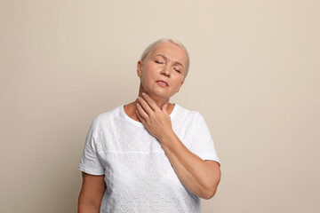 Wall Mural - Mature woman doing thyroid self examination on beige background