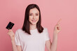 © Tetiana - Photo of young pretty girl hold bank card point finger empty space ad promo select sale isolated over pink color background