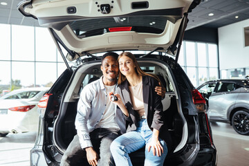 Wall Mural - Couple sitting in open trunk of new auto and holding keys