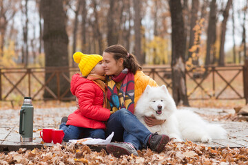 Wall Mural - mom and  child daughter walk with a dog and  drinking hot tea from thermos in autumn park.
