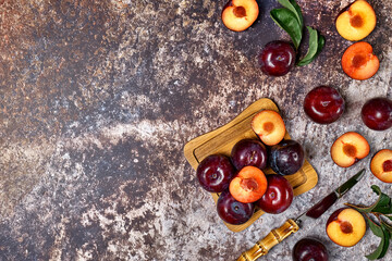 Wall Mural - Ripe purple plum fruits with leaves on colorful background top view.  Whole and sliced plums in wooden plate view from above with space for text.