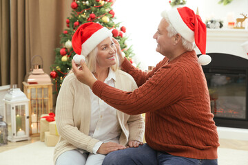 Wall Mural - Happy mature couple in Santa hats at home. Christmas celebration