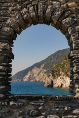 Poster - Vertical shot of the sea and green hills under a blue sky through the arch in Porto Venere