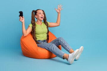 Poster - Full size photo of cool millennial brunette lady sit on chair play station wear jeans t-shirt shoes isolated on blue color background