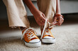 Close up of unrecognizable teenage girl tying laces on bright orange sneakers, copy space