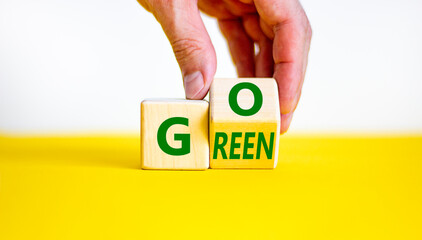 Ecology and go green symbol. Businessman turns a wooden cube with concept words 'Go green' on a beautiful yellow table, white background. Copy space. Business and go green concept.