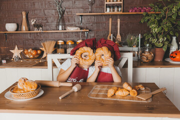 funny kids are preparing dough, baking cookies in the kitchen. Little cooks in aprons hold Easter cakes near their eyes.