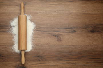 Rolling pin and flour on wooden table, top view. Space for text