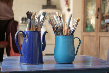 Various professional paint brushes in the blue metal jar on a blurred studio background, selective focus