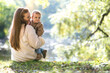 A young mother with a one-year-old baby in an autumn park hugs on the edge of the lake and smile. Filmed from the back
