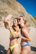 Attractive female friends making selfie at beach party. Two women in colorful swimsuits, smiling, looking at mobile phone. Party, outdoor activity, friendship concept