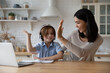 © fizkes - Excited gen z schoolkid in headphones giving high five to happy mom at laptop. Mother helping son to do school home work, giving praise and support for studying achievement. Parenthood, homeschooling