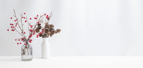 Christmas, New Year home decor. Branches with red berries in a glass vase on a light background. Mock up for displaying works