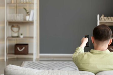 Poster - Man with remote control watching TV on sofa at home