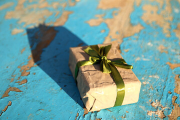 Wall Mural - Wrapped vintage gift box with olive silk ribbon bow on blue (turquoise) old wooden background. Present box in craft paper with green bow with shadow. Holiday concept. Close-up. Side view