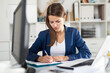 Portrait of busy female entrepreneur sitting at office desk with papers and laptop ..