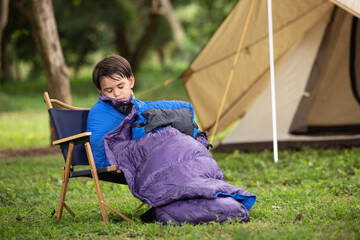 A cute boy preparation sleeping bag near the tent in the forest.