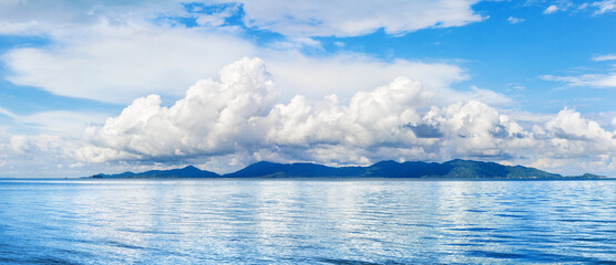 Koh Phangan wide panoramic view from Koh Samui, Thailand. Beautiful tropical island landscape, blue sea water waves, sunny sky, white cumulus clouds, summer holidays vacation travel, seascape panorama