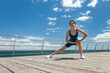 © splitov27 - Fit woman practicing warm-up before training on the embankment at bright sunny day with blue sky and clouds. Wide angle