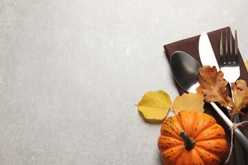 Cutlery, autumn leaves and pumpkin on light grey table, flat lay. Space for text