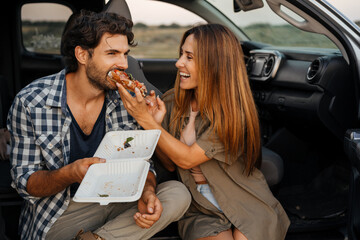 White couple smiling and eating sandwich while sitting in their car