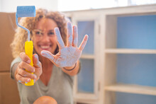 Smiling Woman With Paint Roller And Blue Paint On Hand At Home