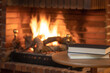 © josemiguelsangar - Books stacked on a small table in front of a fireplace with fire in winter.