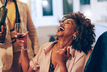 Smiling Happy African Lady At Table - African American Woman Laughing At Party - Young Female Person Holding Glass Of Wine At Dinner