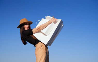 Retail, consumerism or sale concept - luxury fashion styled caucasian woman in brown trousers and hat with bunch of white shopping bags on blue sky background. High quality photo